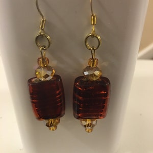 May include: A pair of gold dangle earrings with brown glass beads and clear crystal accents.