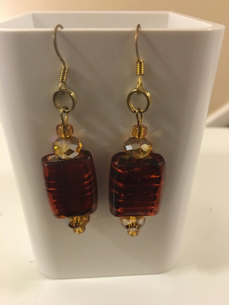 May include: A pair of gold dangle earrings with brown glass beads and clear crystal accents.