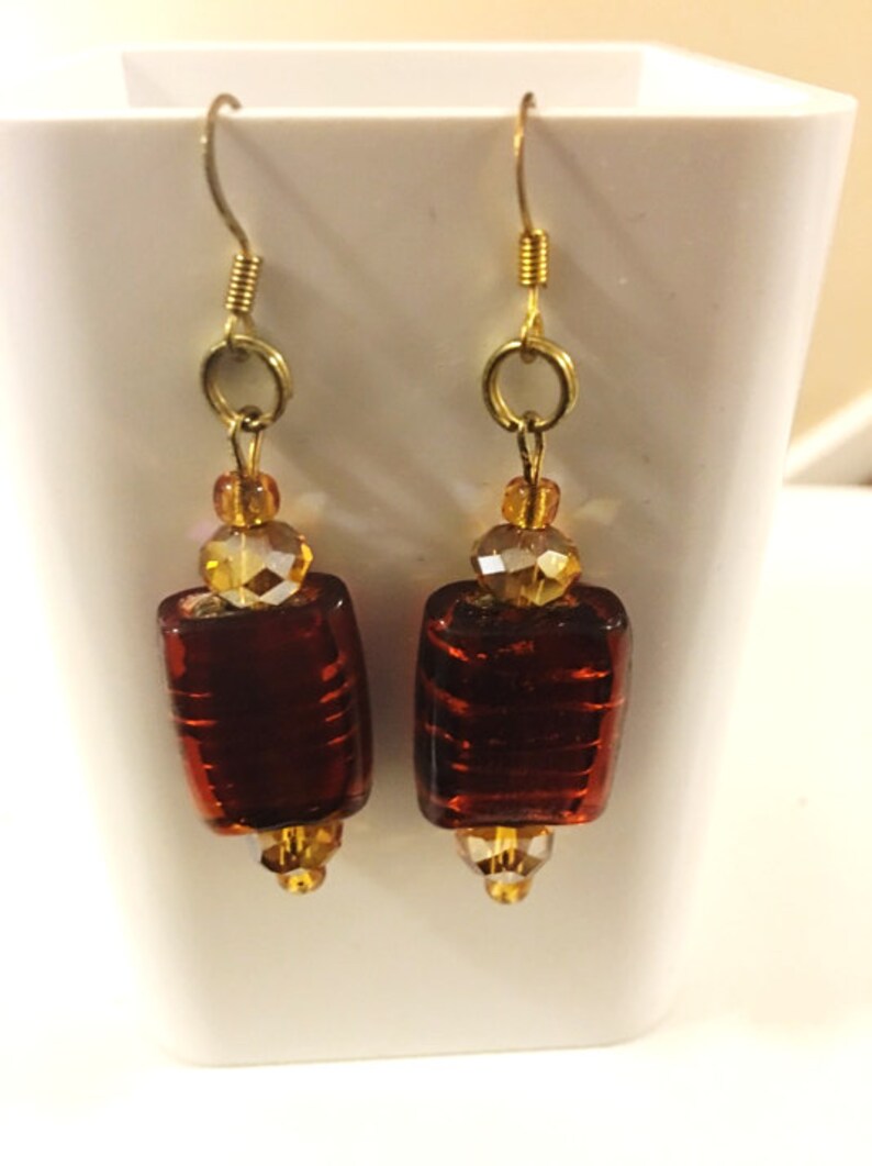 May include: A pair of gold dangle earrings with amber glass beads and a brown glass rectangular bead on each earring.