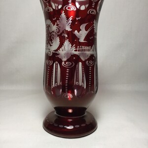 May include: A red glass vase with a white etched design of a bird and flowers. The vase has a round base and a cylindrical body.