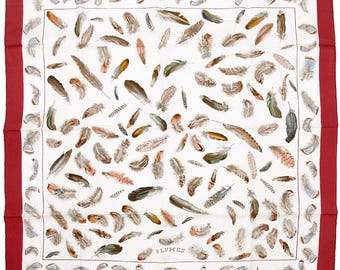 May include: A square silk scarf featuring a white center field decorated with a scattered pattern of various bird feathers in shades of brown, gray, and green. The scarf has a wide, solid dark red border and includes the text PLUMES and HERMES PARIS.