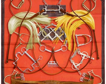 May include: A red silk scarf with a design of various horse riding equipment, including bridles, reins, and a whip. The scarf features the text "HERMES PARIS" in a white rectangle.