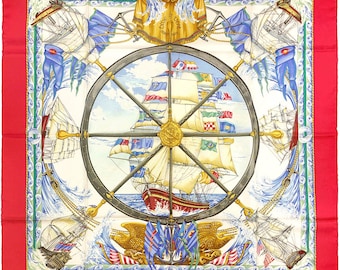 May include: A square silk scarf featuring a central dark gray ship wheel over a large sailing vessel with colorful flags. The design includes four smaller ships in the corners, golden eagle motifs, and a wide red border with a green wave pattern.