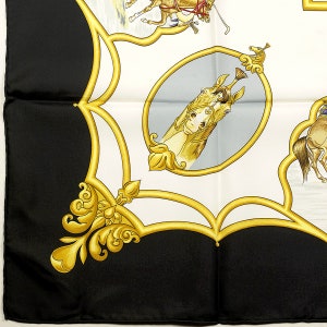 May include: A close-up of a black and white patterned scarf with a gold design. The scarf features a horse's head in a gold oval frame with a blue background. The horse's head is facing right. The scarf is made of silk and has a luxurious feel.