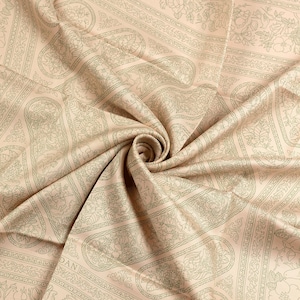 May include: A close-up of a beige fabric with a detailed paisley pattern in a lighter beige color. The fabric is folded and draped, creating a swirl in the center. The pattern includes floral and geometric elements.