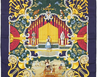 May include: A vintage silk scarf with a colorful illustration of a street organ with musicians and a crowd of people. The design is framed by a decorative border with gold accents. The scarf is navy blue with a repeating pattern.
