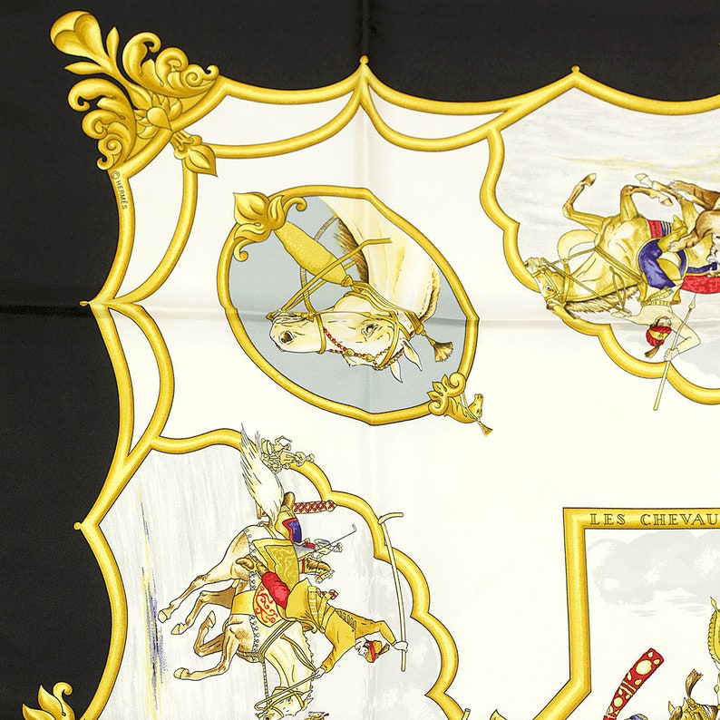 May include: A white and gold silk scarf with a black background. The scarf features a repeating pattern of horses and riders in a variety of poses. The horses are white and the riders are wearing colorful clothing. The scarf is trimmed with a gold border and has the word 'LES CHEVAUX' in gold lettering.