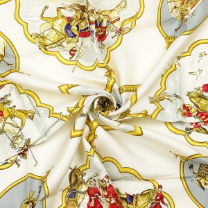 May include: A white silk scarf with a repeating pattern of gold and blue ornate frames. The frames contain images of people riding horses in a variety of poses. The scarf is folded and twisted, showing the pattern in a variety of angles. The text 'MOCHOT' is visible in one of the frames.