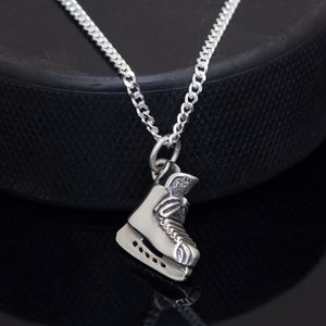 May include: A silver necklace with a detailed ice skate charm. The chain is a curb style and the skate charm is detailed with laces and blades.