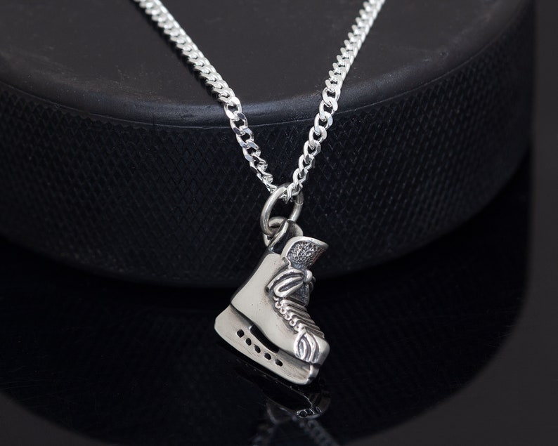 May include: A silver necklace with a detailed ice skate charm. The chain is a curb style and the skate charm is detailed with laces and blades.