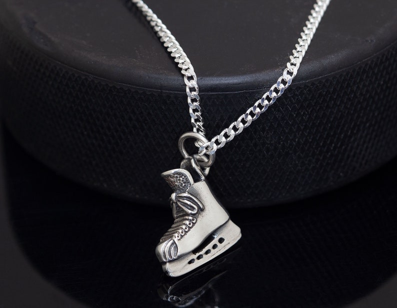 May include: A silver necklace with a silver ice skate charm. The necklace is on a black surface.