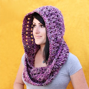 May include: Purple and white crocheted hooded scarf with a textured pattern. The scarf is worn by a person with long black hair.