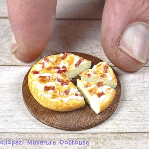 Può includere: Una pizza in miniatura con una crosta bianca e condimenti rossi e bianchi è tagliata in quattro pezzi e disposta su un piatto di legno. La pizza è su una superficie di legno bianco.
