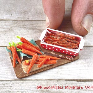 Può includere: Una scena da cucina in miniatura per una casa delle bambole con un tagliere di legno, un coltellino e una ciotola di carote arrostite. Ci sono anche carote crude sul tagliere.