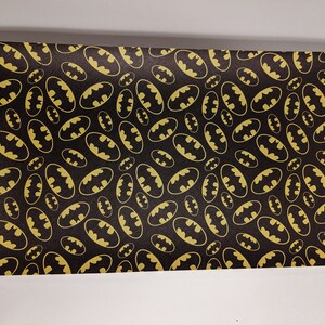May include: Black fabric with a repeating pattern of gold Batman logos.
