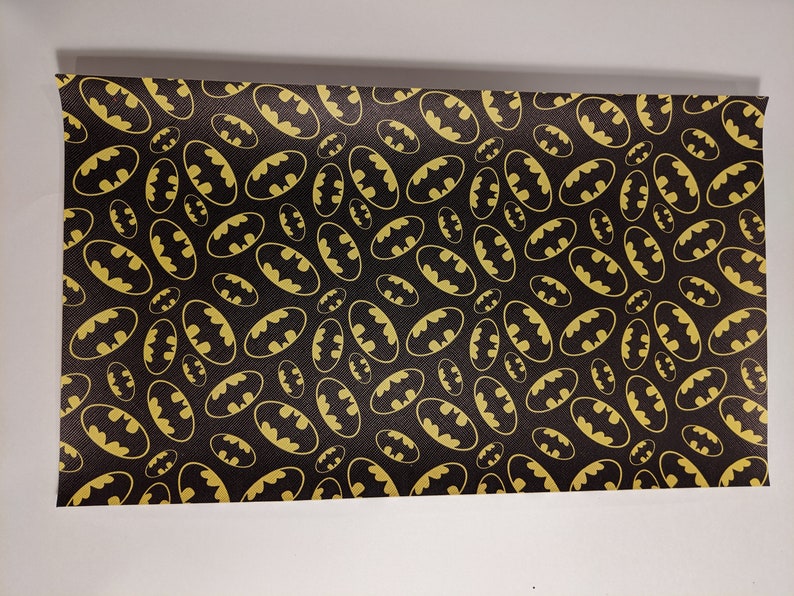 May include: Black fabric with a repeating pattern of gold Batman logos.