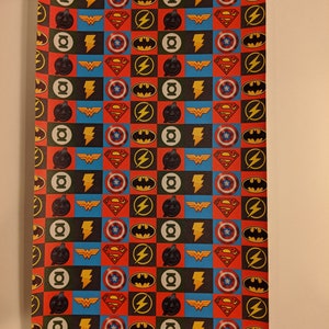 May include: A sheet of wrapping paper with a repeating pattern of superhero logos. The logos include Superman, Batman, Wonder Woman, The Flash, and Green Lantern. The logos are in a checkered pattern of red, blue, yellow, and black.