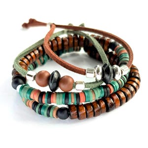 May include: Stacked bracelets featuring wooden beads, leather cords, and colorful accents. The bracelets include brown, green, and black beads, with silver-toned metal spacers. The design incorporates a mix of textures and colors for a layered look.