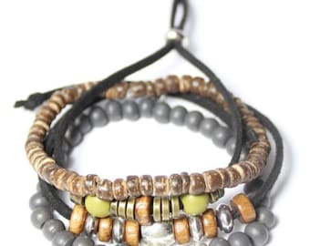 May include: A stack of four bracelets with a bohemian style. The bracelets feature a mix of materials, including wooden beads, gray beads, metal accents, and a black cord. The color palette includes brown, gray, silver, and olive green.