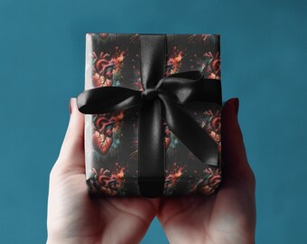 May include: A rectangular gift box wrapped in black paper featuring a repeating anatomical heart pattern with red, orange, and blue watercolor-style accents, tied with a smooth black satin ribbon bow centered across the front surface.