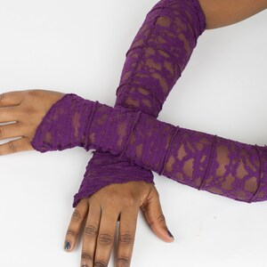 May include: A pair of long, purple lace arm warmers. The arm warmers are made of a delicate, stretchy lace fabric and have a ruffled edge.