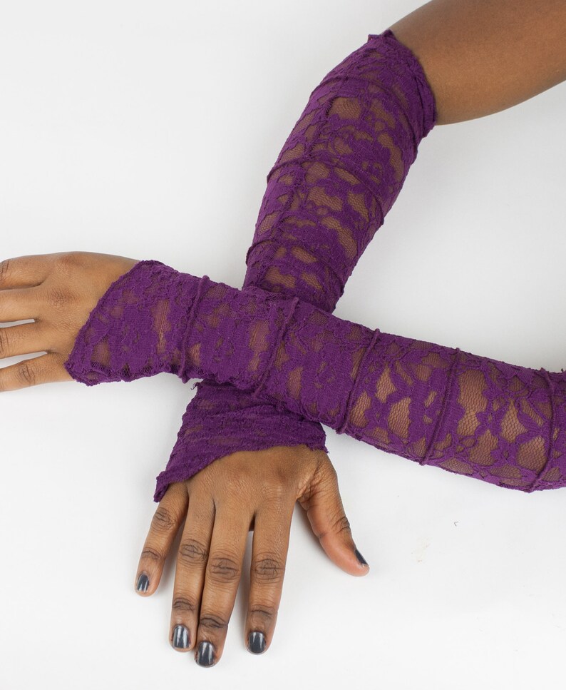 May include: A pair of long, purple lace arm warmers. The arm warmers are made of a delicate, stretchy lace fabric and have a ruffled edge.
