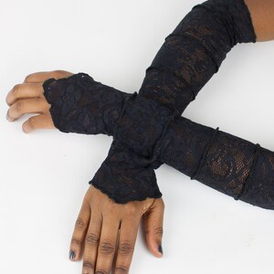 May include: A pair of black lace fingerless gloves. The gloves are long and extend past the elbows. The gloves are made of a delicate lace fabric.