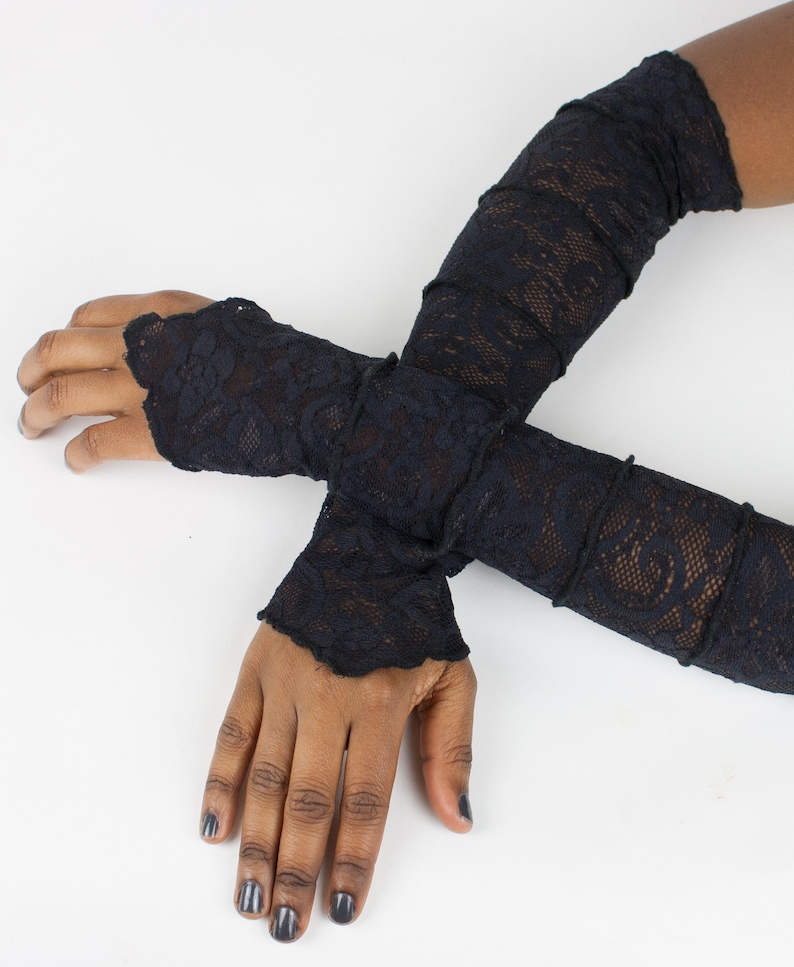 May include: A pair of black lace fingerless gloves. The gloves are long and extend past the elbows. The gloves are made of a delicate lace fabric.