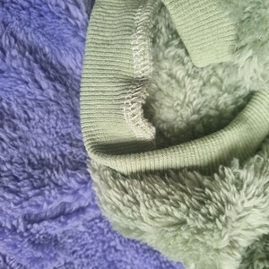 May include: Close-up of a green fleece fabric with a ribbed knit trim. The fabric is soft and fluffy, and the trim is a contrasting color.