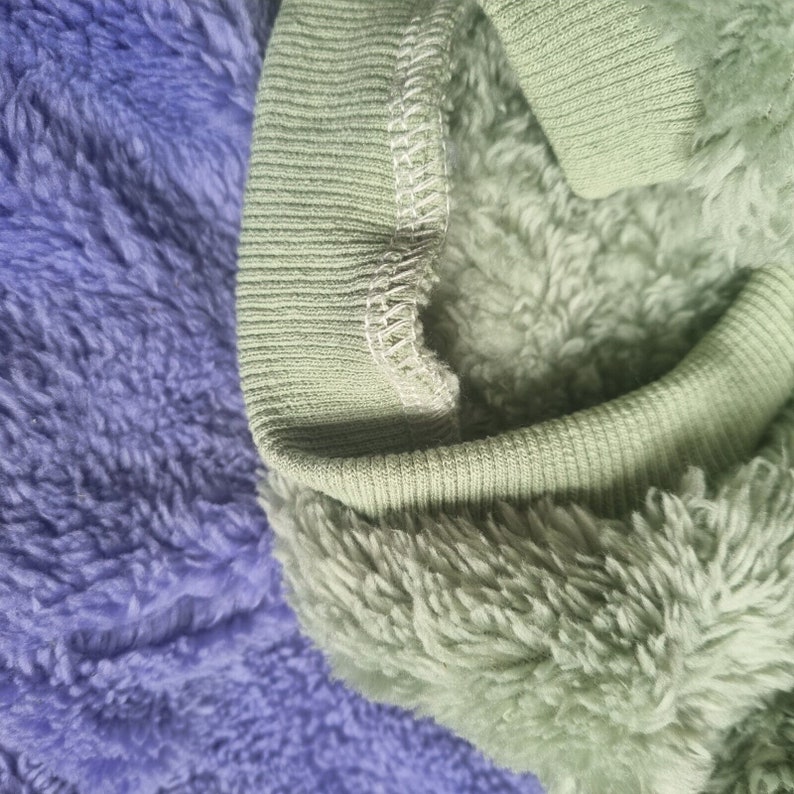 May include: Close-up of a green fleece fabric with a ribbed knit trim. The fabric is soft and fluffy, and the trim is a contrasting color.