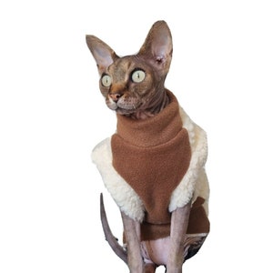 May include: A hairless cat wearing a brown and white fleece sweater. The cat is sitting on a white background.