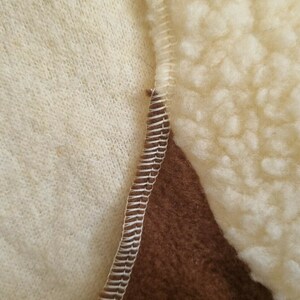 May include: Close-up of a brown, white, and cream colored fabric with a zig-zag stitch seam. The fabric has a fuzzy texture.