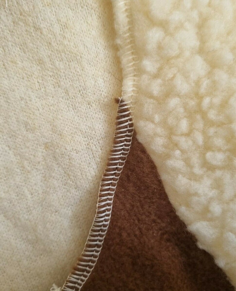 May include: Close-up of a brown, white, and cream colored fabric with a zig-zag stitch seam. The fabric has a fuzzy texture.