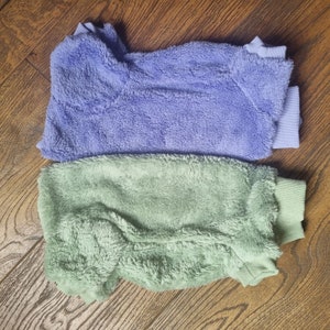 May include: Two soft, fuzzy sweaters, one in a light lavender color and the other in a pale green color. Both sweaters have a ribbed knit collar and cuffs.