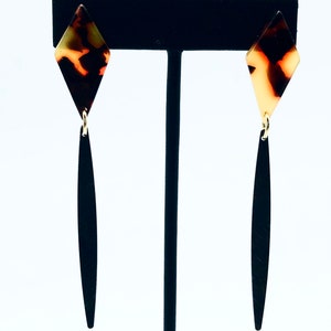 May include: A pair of dangle earrings with a black and brown tortoiseshell diamond-shaped top and a long black dangle.