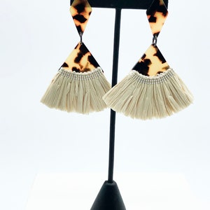 May include: A pair of dangle earrings with a brown and white tortoiseshell pattern on the top and a white fringe on the bottom.