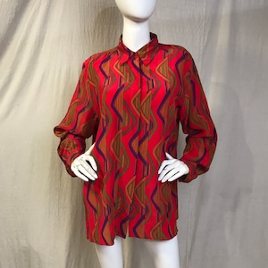 May include: A long-sleeved red blouse with a vibrant, wavy pattern in shades of brown, purple, and green. The blouse has a classic collar and button-down front, displayed on a mannequin. The fabric appears to be lightweight.