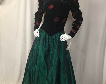May include: A vintage formal dress with a black velvet bodice featuring red rose appliques and long sleeves. The skirt is a vibrant green taffeta, creating a full, flowing silhouette. The dress is displayed on a mannequin.