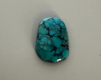 May include: A polished, oval-shaped turquoise gemstone with a mottled pattern of deep teal and black veins. The stone has a glossy finish and is set against a neutral gray background. The gemstone is a natural stone.