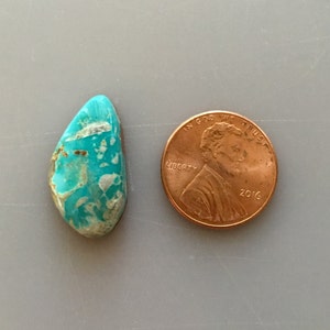 May include: A turquoise cabochon gemstone with a blue-green color and brown matrix. The stone is about the size of a US penny.