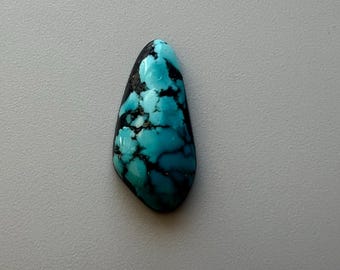 May include: A polished, teardrop-shaped turquoise gemstone with a striking pattern of blue and black veining. The stone is set against a neutral background, highlighting its natural beauty. This gemstone is ideal for jewelry making.