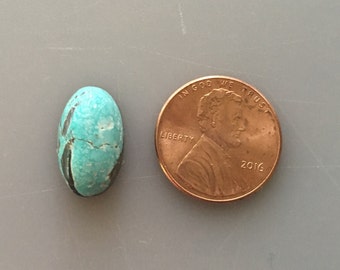 May include: A turquoise cabochon gemstone with black veins and a rough texture. The gemstone is oval-shaped and is about the size of a US penny.