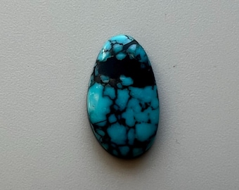 May include: A polished, oval-shaped gemstone with a striking pattern. The stone features a vibrant turquoise base color, intricately veined with dark black patterns. The gemstone is smooth and appears to be a natural stone.