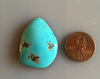 May include: A turquoise cabochon gemstone with brown matrix, approximately the size of a US penny.
