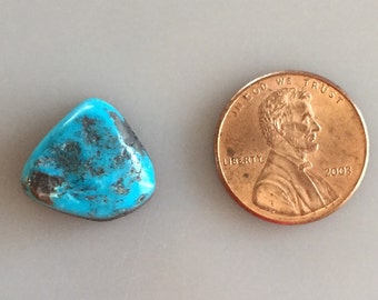 May include: A turquoise cabochon gemstone with a dark blue and black matrix. The stone is approximately the size of a US penny.