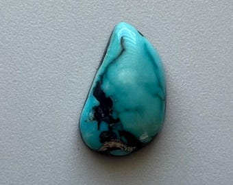 May include: A polished, teardrop-shaped turquoise gemstone with dark matrix veining. The stone's surface is a vibrant, saturated teal color, with areas of black and brown. The gemstone is set against a neutral gray background.