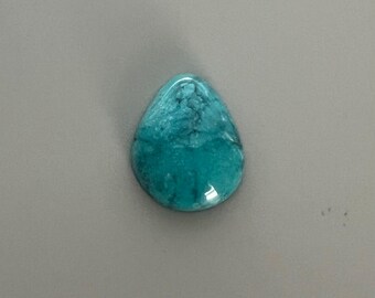 May include: A teardrop-shaped turquoise gemstone with a polished surface. The stone displays a mottled pattern of light and dark blue-green hues. The gemstone is set against a neutral gray background.