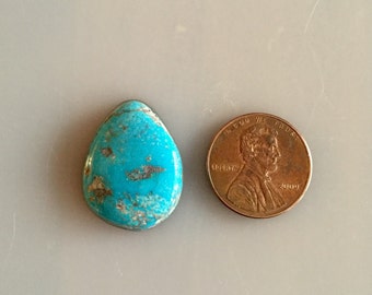 May include: A turquoise cabochon gemstone in a teardrop shape, next to a US penny for size comparison.