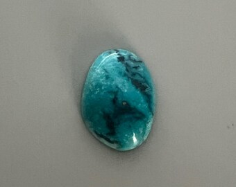 May include: A polished, oval-shaped gemstone with a vibrant teal color and dark blue veining. The stone has a smooth, glossy surface and is set against a neutral gray background. This gemstone could be used for jewelry making or as a decorative element.