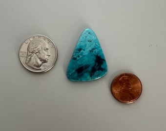 May include: A turquoise gemstone with black veining, next to a U.S. quarter and a penny. The gemstone is a triangular shape with a polished surface. The quarter shows George Washington and the year 2022.